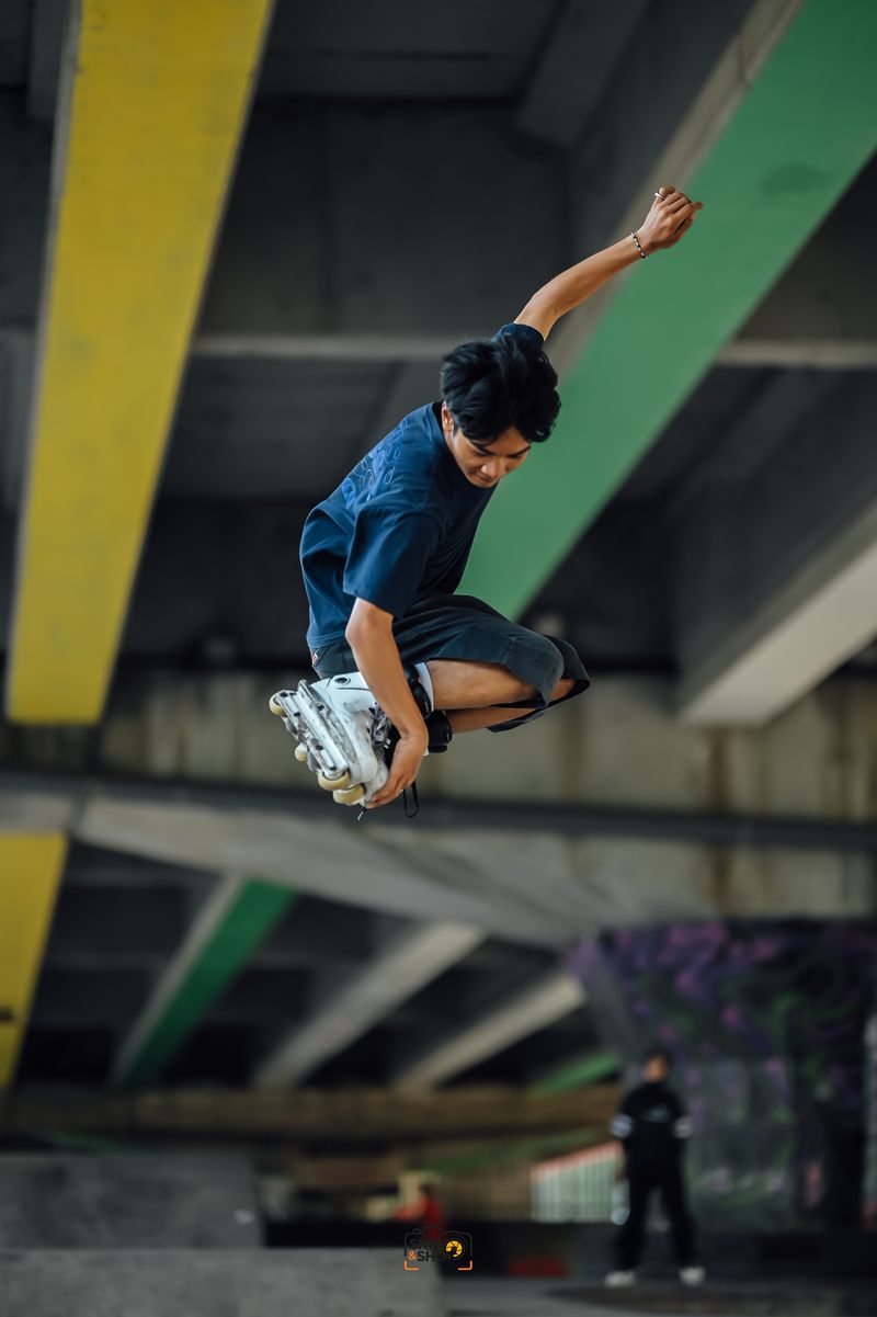 Inline skater grabbing a skate in mid-air beneath colorful concrete beams