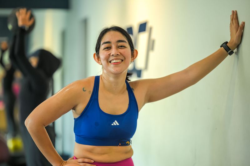 Smiling athlete in a blue training top resting one hand against a gym wall