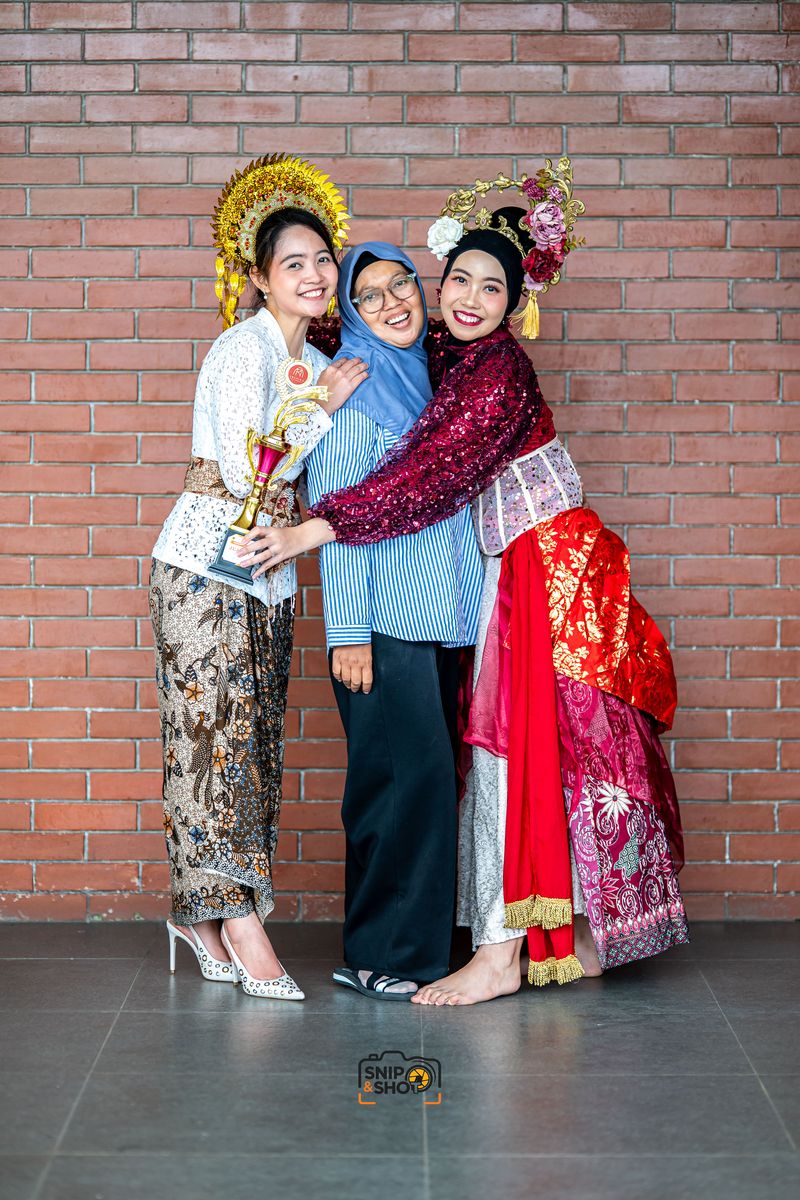 Three smiling women posing together, two wearing traditional dance costumes