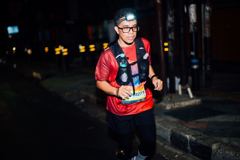 Runner in a red shirt and hydration vest beneath city lights at night