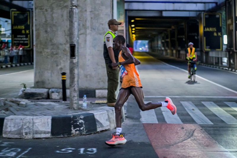 Runner in an orange singlet crossing a city intersection in full stride