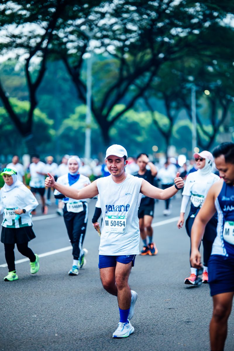 Runner with both arms outstretched amid a group on a tree-lined road