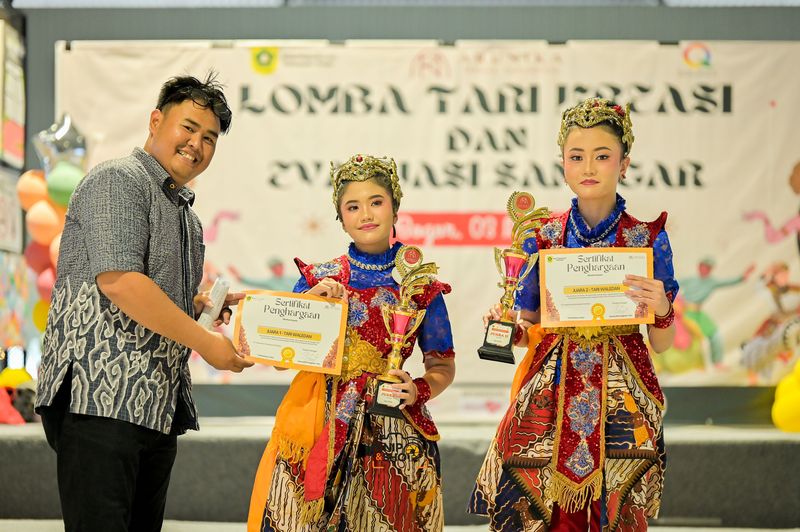 Two dancers holding trophies and certificates beside an adult at an event