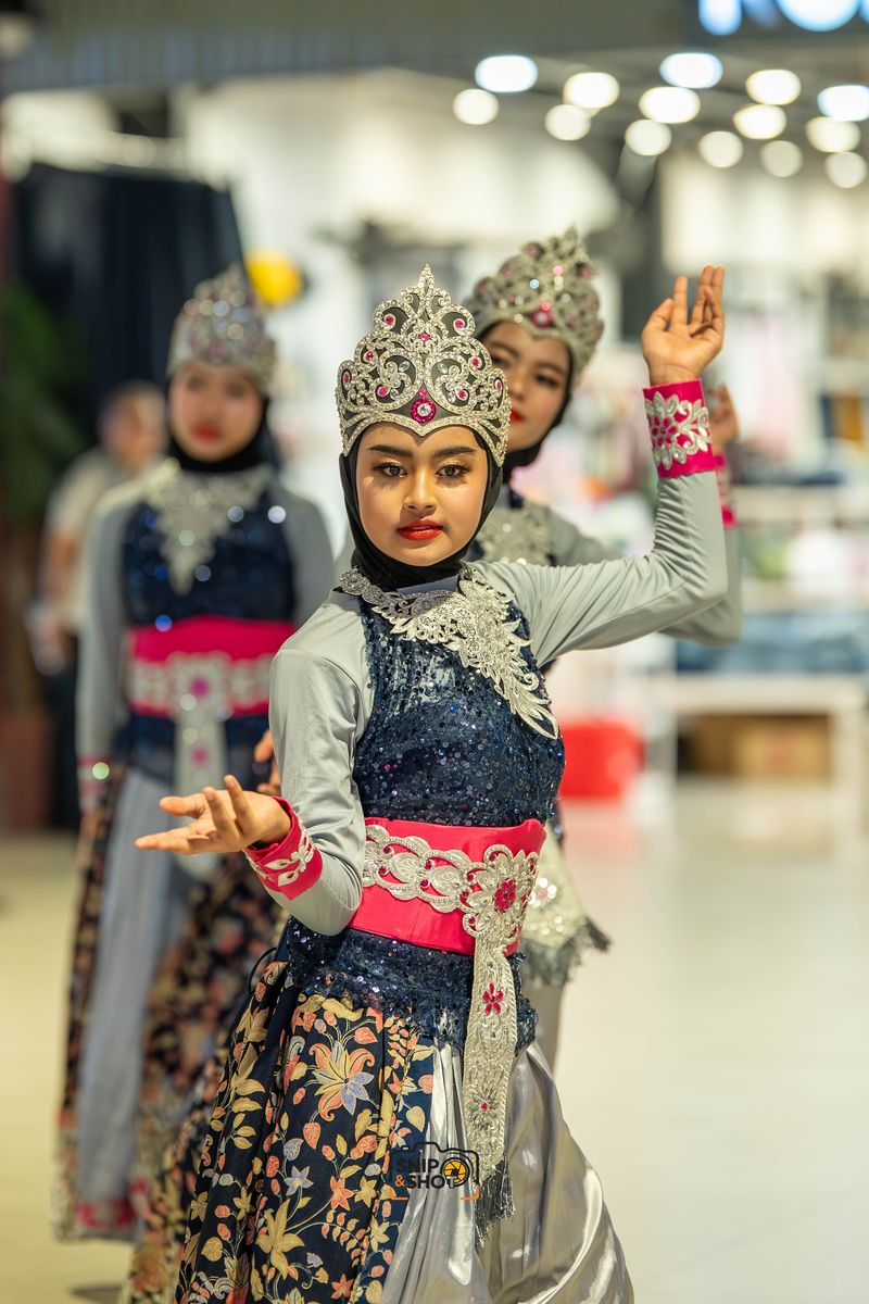 Dancers in ornate silver headdresses and dark costumes holding hand gestures